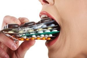 женщина засовывает в рот упаковки таблеток